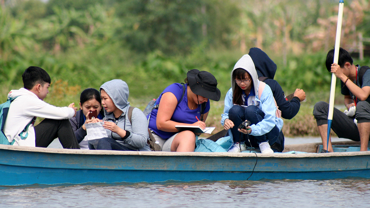 Students testing water, together in a river boat, in Vietnam