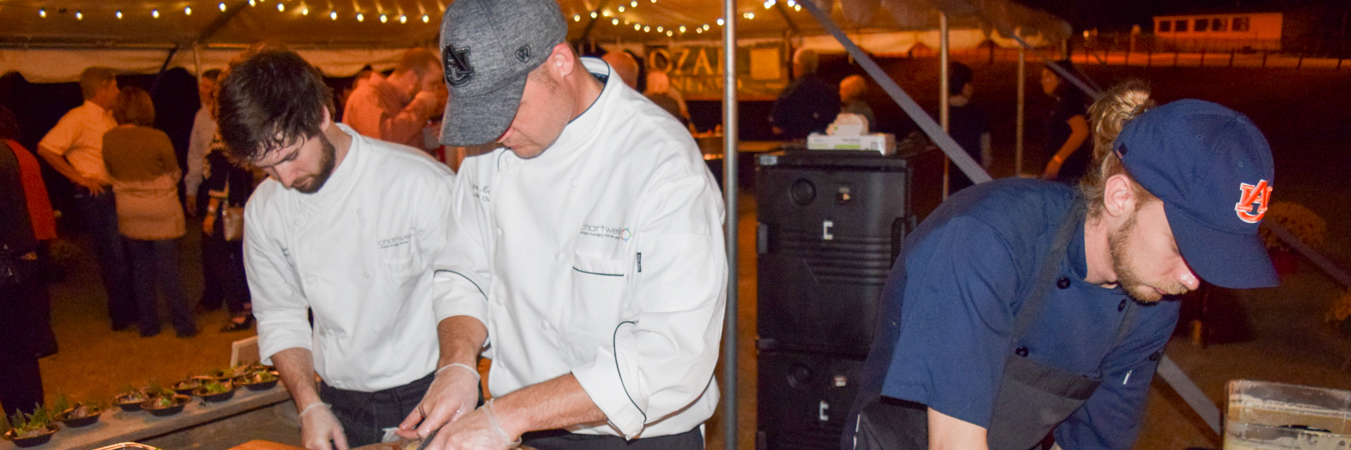 Three chefs, one wearing an Auburn cap, cooking at the Birds n Brews College of Agriculture event