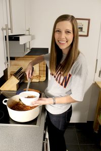 Beth Westmoreland Miller, Auburn University Food Science alumni, cooking some southern chili meal in her kitchen holding a white bowl of fresh hot chili.