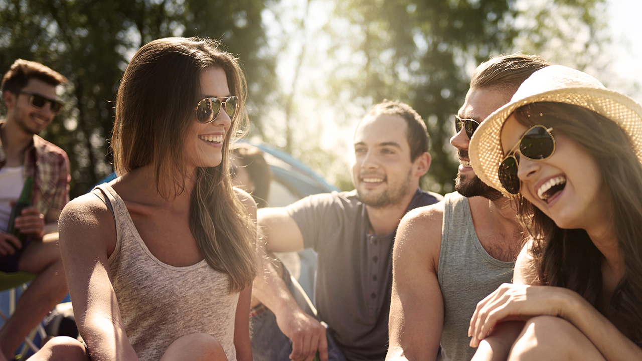 Student Clubs, College group of friends talking and laughing outdoors on the beach, wearing sunglasses, straw hat, trees in the bg