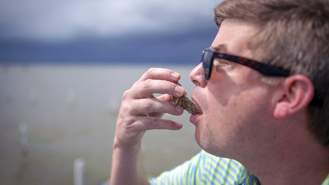 Close-up-of-man-eating-oyster-wearing-sun-glasses-beach-dock