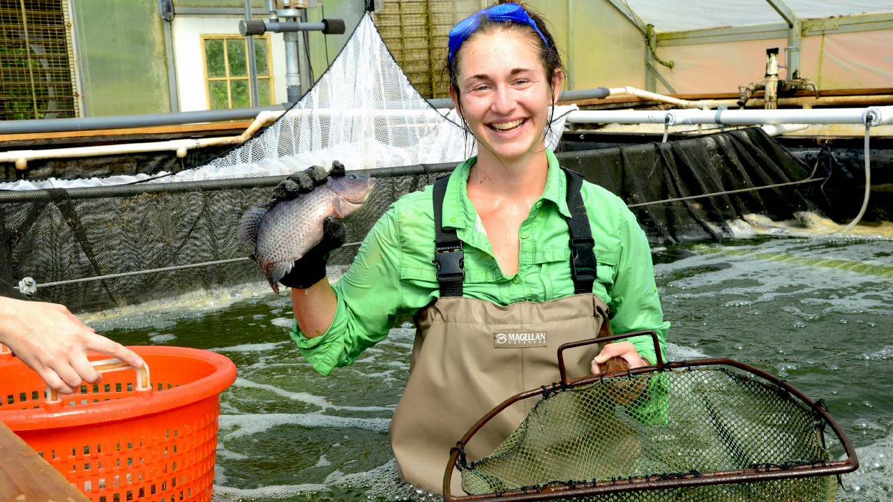 Smiling college student holding fish and net Minor in Fisheries, Aquaculture & Aquatic Science Undergraduate Minor Degree