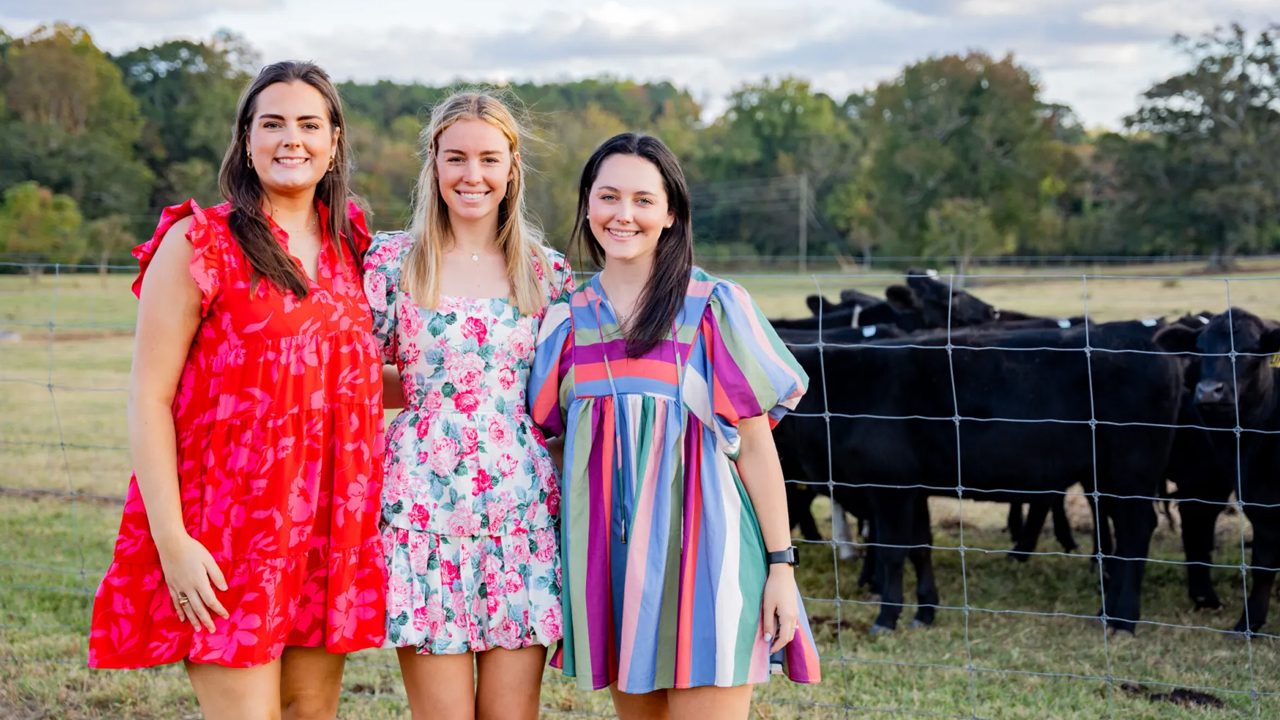 3 female students smile and pose in front of cattle