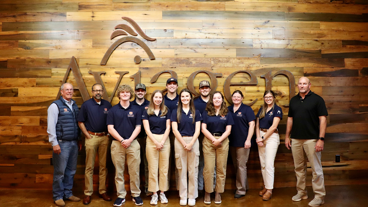 Group of Auburn students, faculty and staff stand in front of wall with Aviagen logo