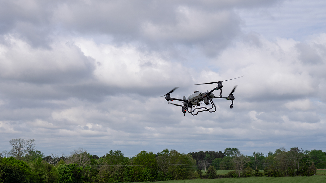 A drone flies over a field on a cloudy day