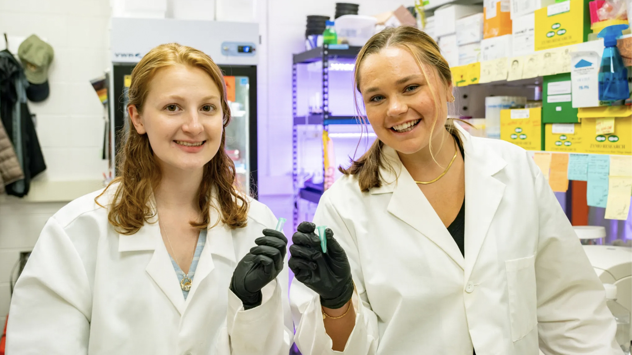 Two students hold test tubes while inside a lab