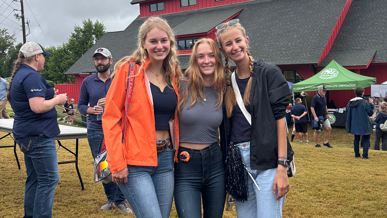 Three young women smile in front of the red barn at Ag Heritage Park at the 2024 Ag Roundup